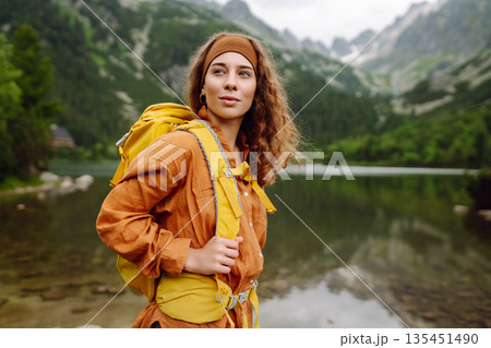 Travel Slovakia, Europe. Tourist with a yellow backpack stands against the backdrop of alpine lake. 135451490