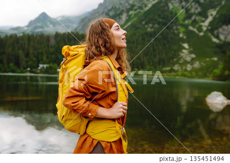 Travel Slovakia, Europe. Tourist with a yellow backpack stands against the backdrop of alpine lake. 135451494