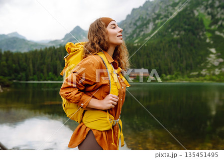 Travel Slovakia, Europe. Tourist with a yellow backpack stands against the backdrop of alpine lake. 135451495