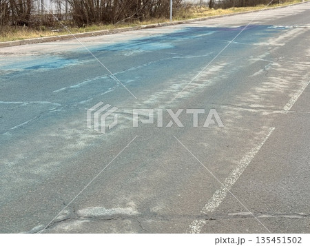 A Blue Chemical Stain On The Asphalt Of The Road, On Which Uneven Spots Of Bright Blue Liquid Are Visible, Accumulated In Puddles And Smeared On Faded Markings And Cracked Asphalt. A Blue Chemical Stain On The Asphalt Of The Road, On Which Uneven Spots Of Bright Blue Liquid Are Visible, Accumulated In Puddles And Smeared On Faded Markings And Cracked Asphalt. 135451502
