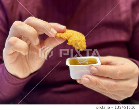 Woman Hand Holding Chicken Nugget Over Sauce, CloseUp Of Casual Eater In Maroon Shirt Dipping Golden Crispy Nugget Into HoneyMustard. Remote Worker Enjoying Quick food. Woman Hand Holding Chicken Nugget Over Sauce, CloseUp Of Casual Eater In Maroon Shirt Dipping Golden Crispy Nugget Into HoneyMustard. Remote Worker Enjoying Quick food. 135451510