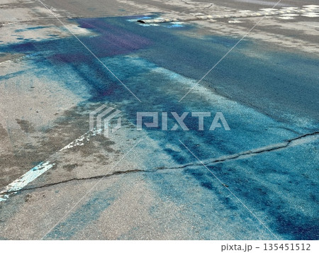 A Blue Chemical Stain On The Asphalt Of The Road, On Which Uneven Spots Of Bright Blue Liquid Are Visible, Accumulated In Puddles And Smeared On Faded Markings And Cracked Asphalt. 135451512