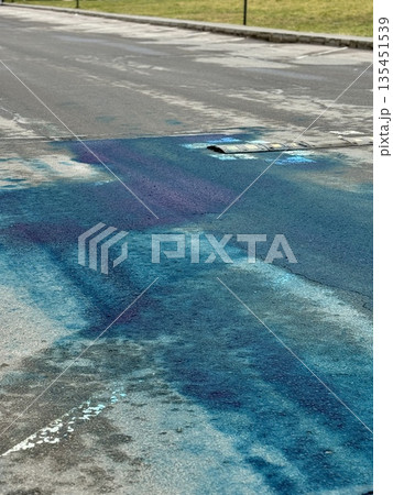 A Blue Chemical Stain On The Asphalt Of The Road, On Which Uneven Spots Of Bright Blue Liquid Are Visible, Accumulated In Puddles And Smeared On Faded Markings And Cracked Asphalt. 135451539