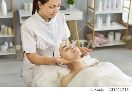 Esthetician performing facial massage for woman client in bright spa treatment room 135451718