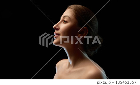 Low key female profile portrait with soft rim lighting. 135452357