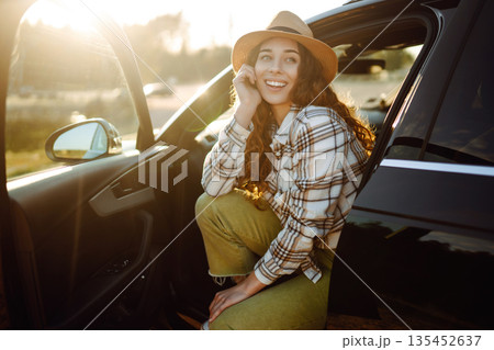 Joyful traveler embraces nature at sunset by lakeside with open car door, freedom, adventure. 135452637