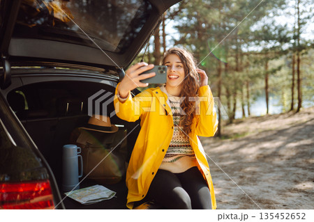 Happy Woman is resting in trunk of car and taking selfie. Travel, tourism, nature, active life. Happy Woman is resting in trunk of car and taking selfie. Travel, tourism, nature, active life. 135452652