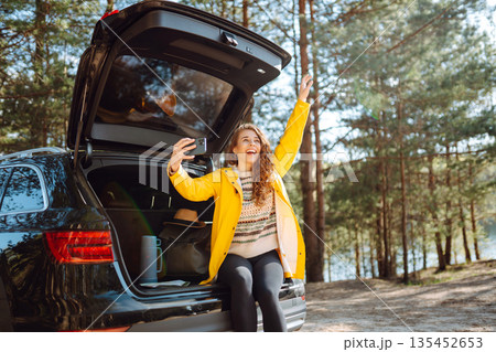 Happy Woman is resting in trunk of car and taking selfie. Travel, tourism, nature, active life. Happy Woman is resting in trunk of car and taking selfie. Travel, tourism, nature, active life. 135452653