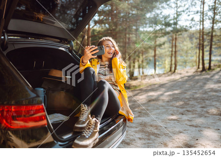 Happy Woman is resting in trunk of car and taking selfie. Travel, tourism, nature, active life. Happy Woman is resting in trunk of car and taking selfie. Travel, tourism, nature, active life. 135452654