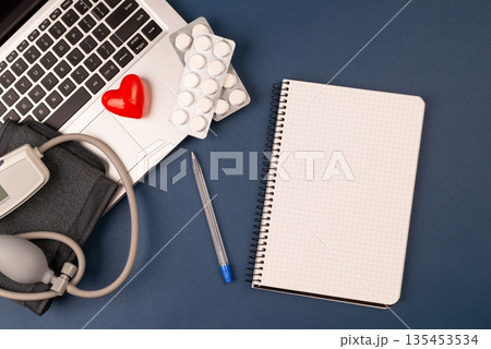 blood pressure meter on laptop with red heart, and pills on dark blue background.paper nootebook with copy space cardiology concept.Tonometer or sphygmomanometer. at the doctor's appointment. top view 135453534