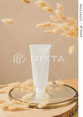 cosmetic tube with face cream, hand cream, body lotion or cleanser on a mirror podium with reflector with dried flowers. The concept of gentle skin care cosmetic tube with face cream, hand cream, body lotion or cleanser on a mirror podium with reflector with dried flowers. The concept of gentle skin care 135453549