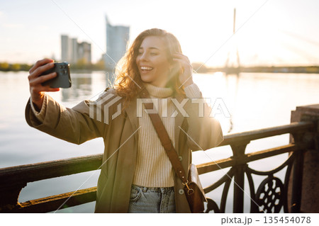 Selfie time. Woman holding mobile phone taking selfie photo, standing on waterfront. Lifestyle. Selfie time. Woman holding mobile phone taking selfie photo, standing on waterfront. Lifestyle. 135454078