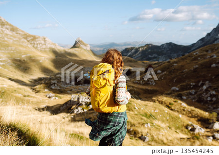 Traveler woman with a bright yellow backpack strolls through golden meadows. Active lifestyle Traveler woman with a bright yellow backpack strolls through golden meadows. Active lifestyle 135454245