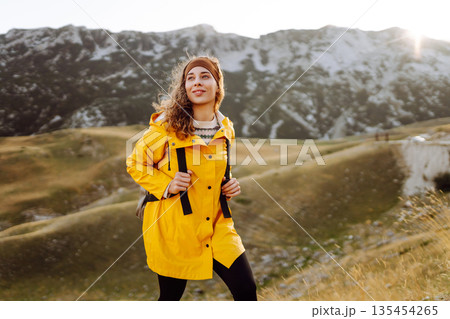 Traveler woman in yellow jacket enjoys hiking on sun. Hiking in mountains with backpacks. Adventure. Traveler woman in yellow jacket enjoys hiking on sun. Hiking in mountains with backpacks. Adventure. 135454265