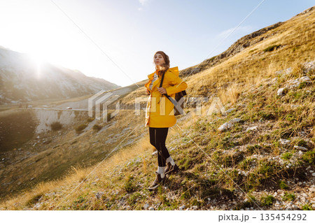 Traveler woman in yellow jacket enjoys hiking on sun. Hiking in mountains with backpacks. Adventure. 135454292