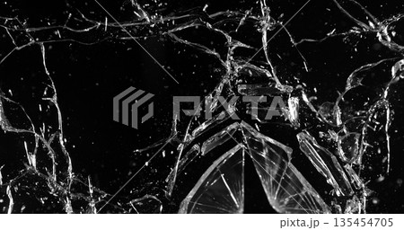 Front view photo of glass shattered by a bullet. Gunshot impact creates cracks, flying shards and dust isolated on black background. Perfect VFX overlay element or dramatic background. Front view photo of glass shattered by a bullet. Gunshot impact creates cracks, flying shards and dust isolated on black background. Perfect VFX overlay element or dramatic background. 135454705