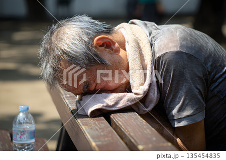 公園のベンチでぐったりと倒れ込む高齢男性 夏の熱中症による意識障害と脱水症状の危険 公園のベンチでぐったりと倒れ込む高齢男性 夏の熱中症による意識障害と脱水症状の危険 135454835