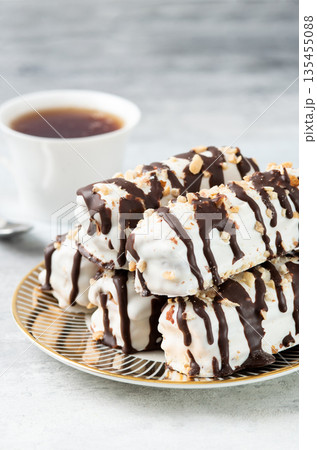 Delicious eclairs with white icing and chocolate drizzle on a decorative plate. Sweet dessert served with coffee. Delicious eclairs with white icing and chocolate drizzle on a decorative plate. Sweet dessert served with coffee. 135455088