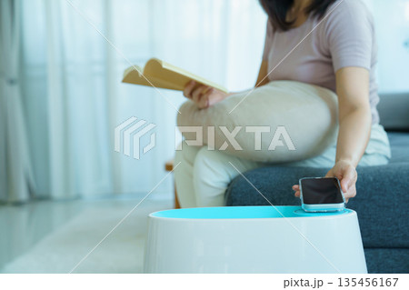 Woman controlling home air purifier or humidifier with smartphone while relaxing at home. 135456167