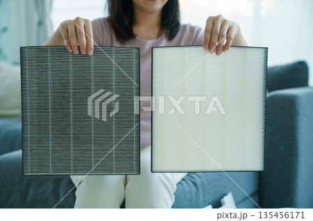 Asian woman showing dirty and clean air purifier filters for comparison. 135456171