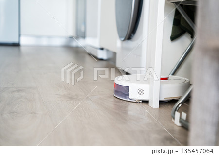 Autonomous robot vacuum cleaner cleaning under kitchen cabinet, smart home appliance for efficient household floor maintenance Autonomous robot vacuum cleaner cleaning under kitchen cabinet, smart home appliance for efficient household floor maintenance 135457064