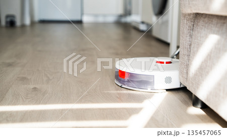 Robot vacuum cleaner cleaning wooden floor under sofa in modern apartment, smart home technology and automated housekeeping concept Robot vacuum cleaner cleaning wooden floor under sofa in modern apartment, smart home technology and automated housekeeping concept 135457065