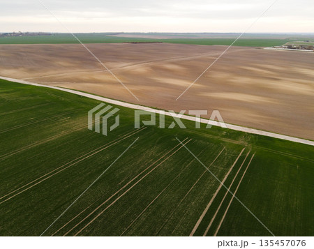 Aerial farmland landscape with green crops, dirt road and plowed fields, rural agriculture scenery from drone Aerial farmland landscape with green crops, dirt road and plowed fields, rural agriculture scenery from drone 135457076
