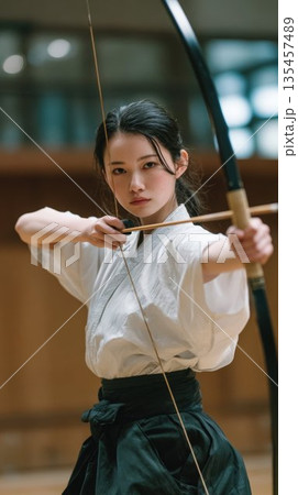 弓道場で静かに精神を統一して的を狙う女子高校生 135457489