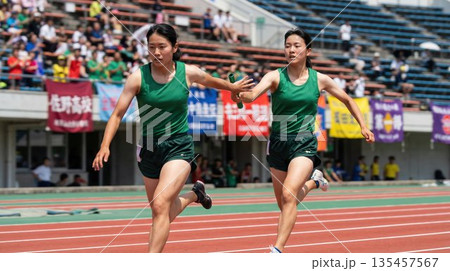 リレー競技でトラックを疾走しバトンパスを行う女子高生ランナー リレー競技でトラックを疾走しバトンパスを行う女子高生ランナー 135457567