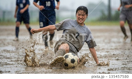 雨のぬかるみの中で激しいスライディングを見せる女子サッカー部員 雨のぬかるみの中で激しいスライディングを見せる女子サッカー部員 135457580