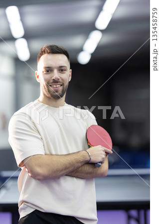 Young man smiling holding table tennis paddle indoors Young man smiling holding table tennis paddle indoors 135458759