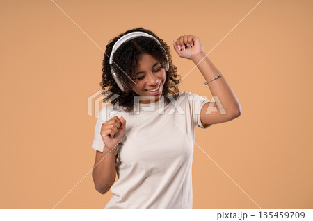 African Teen Girl Listening Music, Enjoying Songs, Headphones On Beige Backdrop African Teen Girl Listening Music, Enjoying Songs, Headphones On Beige Backdrop 135459709