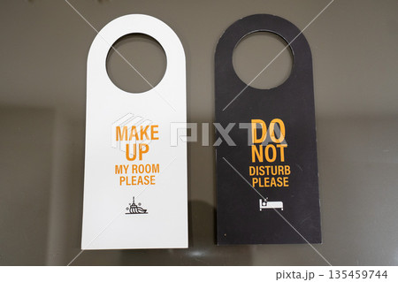 Hotel door hangers with messages Make up my room please and Do not disturb please placed side by side on a neutral surface 135459744