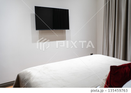 Modern hotel room interior with neatly made bed, wall-mounted TV and minimalistic design in neutral tones. Ideal for concepts of travel accommodation 135459763