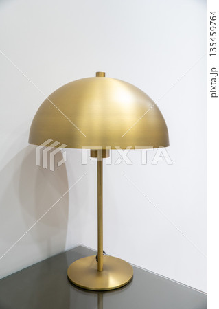 Modern gold metal table lamp with dome-shaped shade standing on a bedside table against a white wall. Suitable for concepts of interior design Modern gold metal table lamp with dome-shaped shade standing on a bedside table against a white wall. Suitable for concepts of interior design 135459764