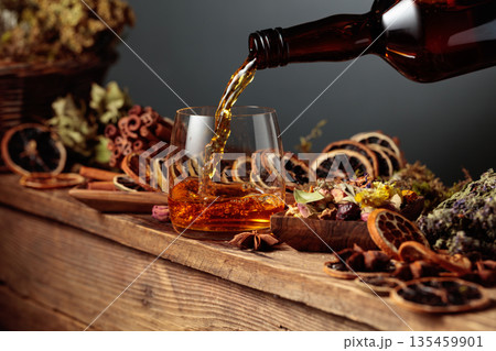 Herbal liquor is poured from a vintage bottle into a glass. Herbal liquor is poured from a vintage bottle into a glass. 135459901