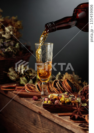 Herbal liquor is poured from a vintage bottle into a glass. Herbal liquor is poured from a vintage bottle into a glass. 135459906
