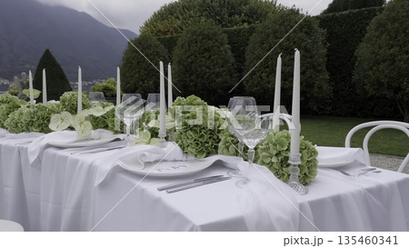 An Elegant Outdoor Dining Setup Featuring Beautiful Greenery and Soft Candlelight. Action 135460341