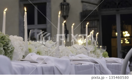 White candles burning on a wedding table set in front of a villa. Action White candles burning on a wedding table set in front of a villa. Action 135460580