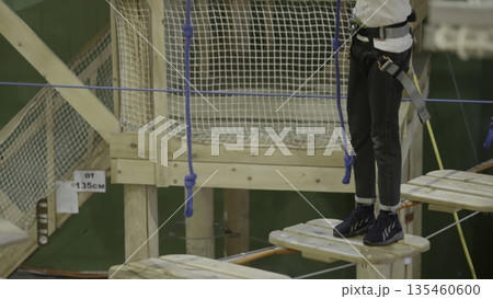 Young girl carefully crossing rope bridge in adventure park. Creative 135460600