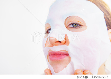 Woman applying sheet mask on face 135460797