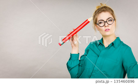 Woman confused thinking, big pencil in hand Woman confused thinking, big pencil in hand 135460896