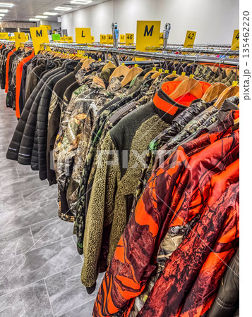 A large retail display of hunting and outdoor jackets, featuring various camouflage and blaze orange patterns, all organized on a clothing rack.. High quality photo A large retail display of hunting and outdoor jackets, featuring various camouflage and blaze orange patterns, all organized on a clothing rack.. High quality photo 135462220