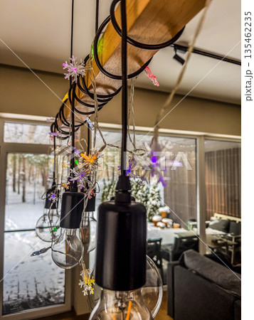 A close-up of a modern, industrial-style light fixture made of wood and metal, decorated for the holidays with colorful snowflake-shaped Christmas lights.. High quality photo 135462235