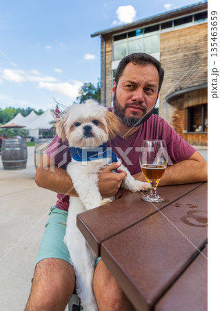 A man is sitting at a table with a dog on his lap A man is sitting at a table with a dog on his lap 135463659