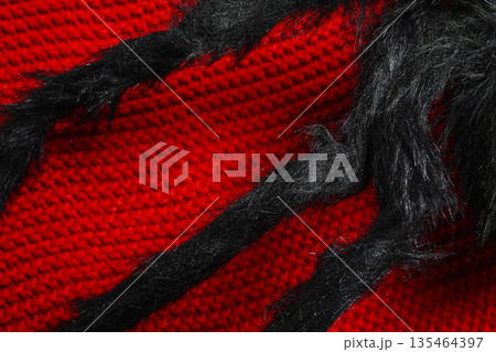 Macro view of a fuzzy black artificial spider toy crawling across a bright red textured knitted sweater. Creative Halloween decoration or scary costume detail background Macro view of a fuzzy black artificial spider toy crawling across a bright red textured knitted sweater. Creative Halloween decoration or scary costume detail background 135464397