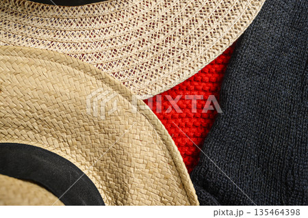 Close-up abstract view showing contrasting textures of straw hats, a bright red knitted sweater, and black woven fabric. Ideal for fashion, textile, and material backgrounds 135464398