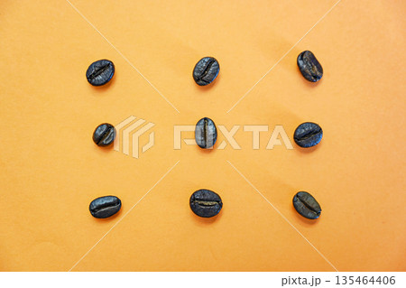 Minimalist flat lay of nine dark roasted coffee beans in a grid on a vibrant orange background. Ideal for cafe branding, caffeine-themed designs, and modern food patterns 135464406