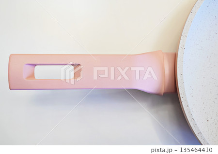 Close-up of a stylish pastel pink handle on a modern ceramic non-stick frying pan, isolated on a white background. Minimalist kitchenware design for contemporary cooking Close-up of a stylish pastel pink handle on a modern ceramic non-stick frying pan, isolated on a white background. Minimalist kitchenware design for contemporary cooking 135464410