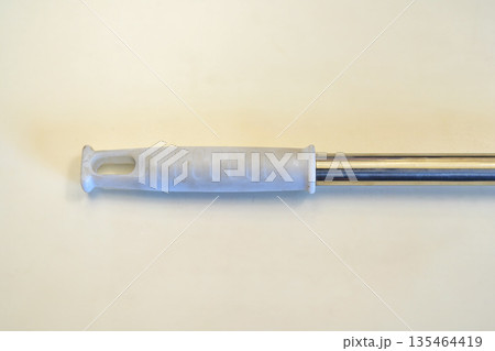 Close-up of a white plastic ergonomic handle attached to a shiny stainless steel rod, used for cleaning tools like mops or brooms, set against a plain light background 135464419